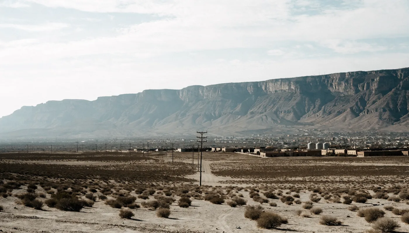 Dry high desert basin with an open utility easement and a pole line running toward a steep mountain escarpment