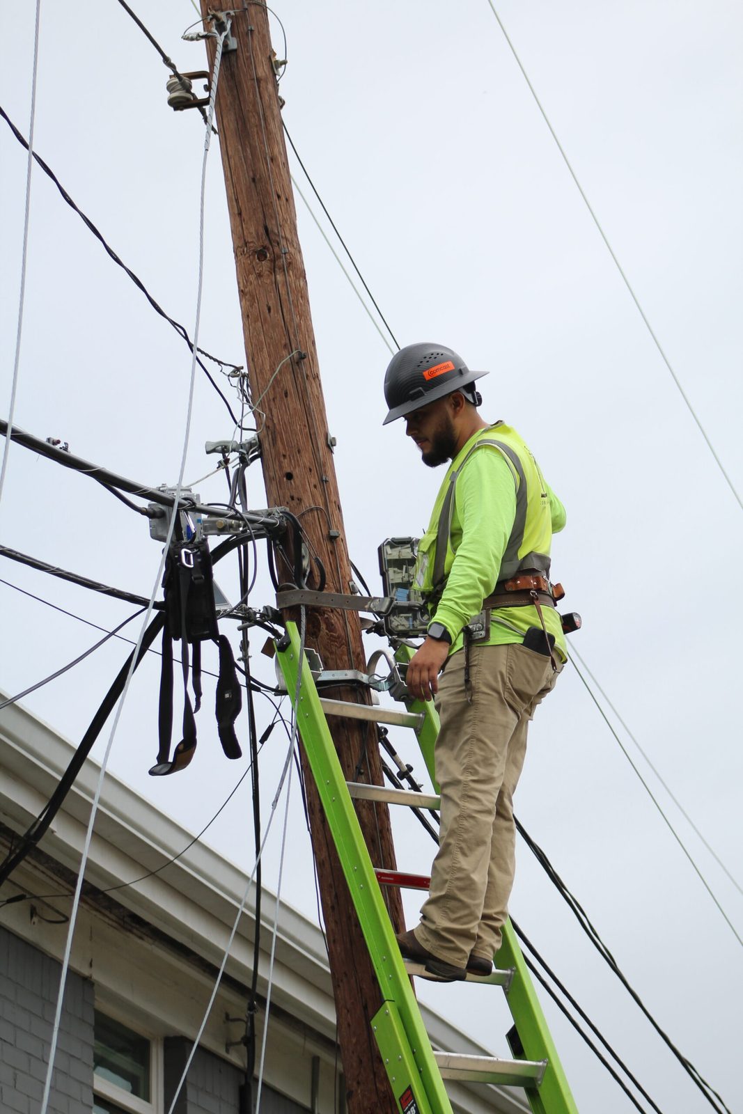 A One World Communications technician working at an enclosure on the pole from a ladder