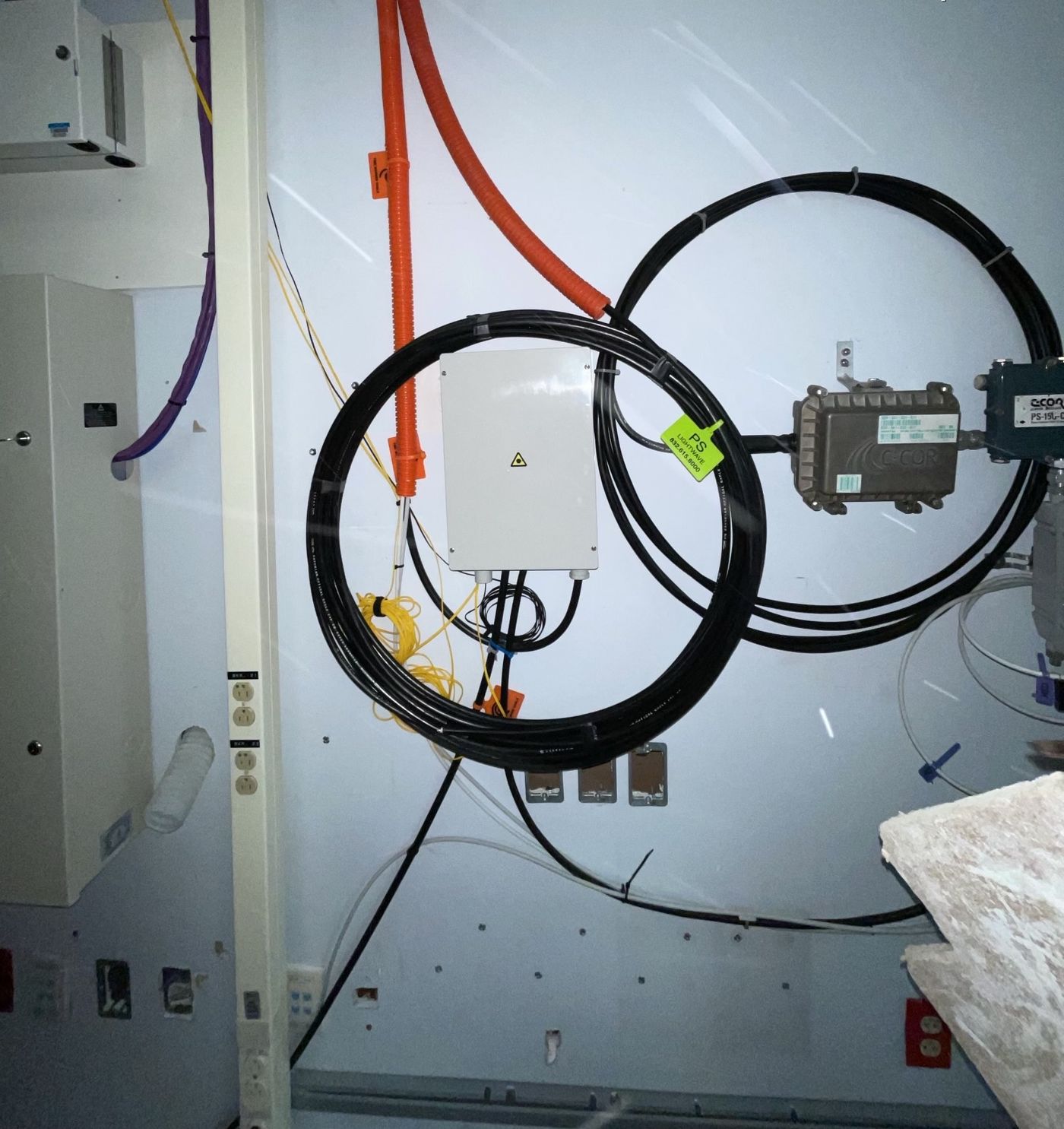 A fiber splice enclosure on a One World Communications job, slack loops dressed and coiled on the wall with the fiber jumpers landed into the box