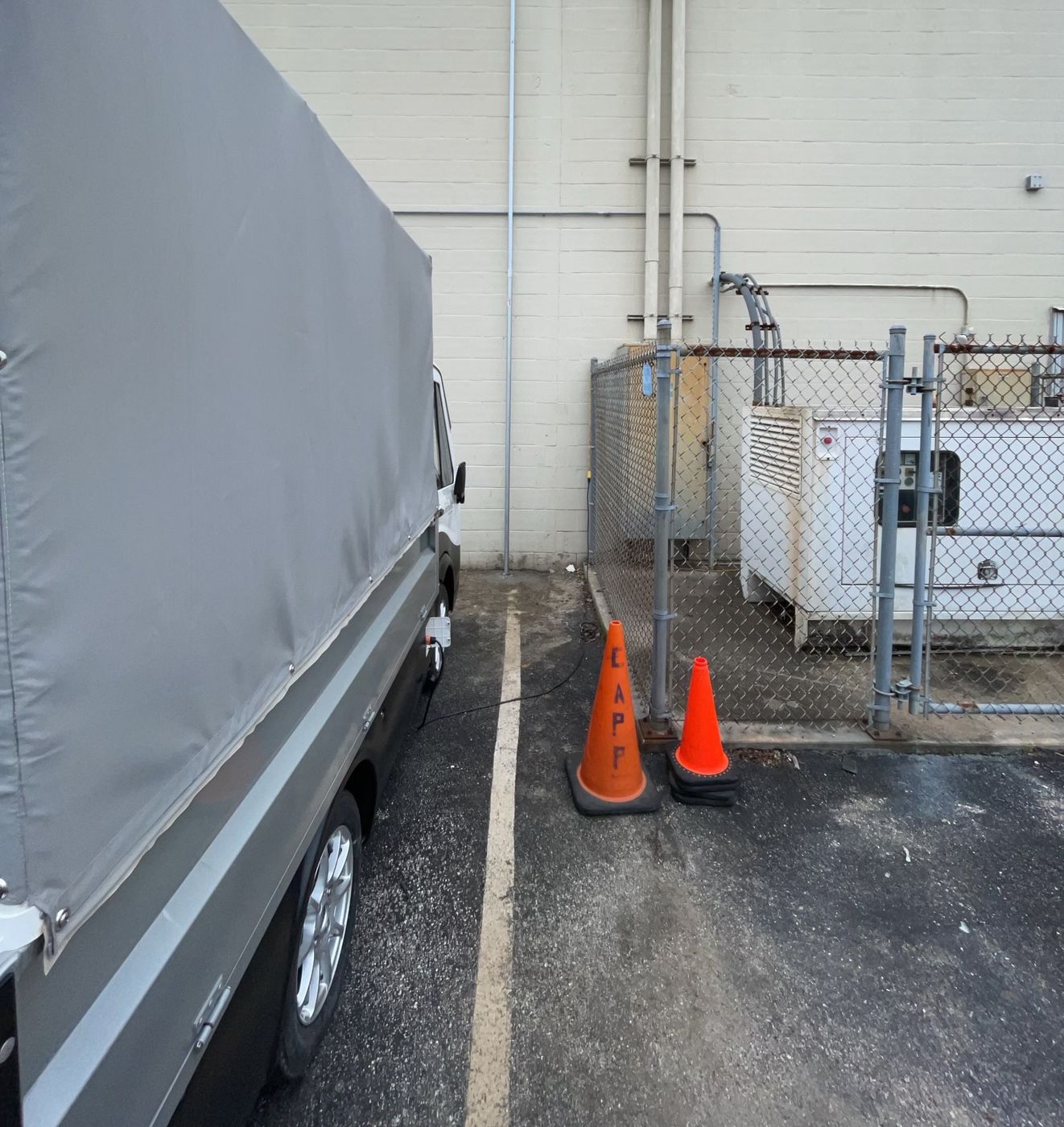 A One World Communications service truck on site at a facility, safety cones set out and a line run from the truck across to the fenced equipment enclosure